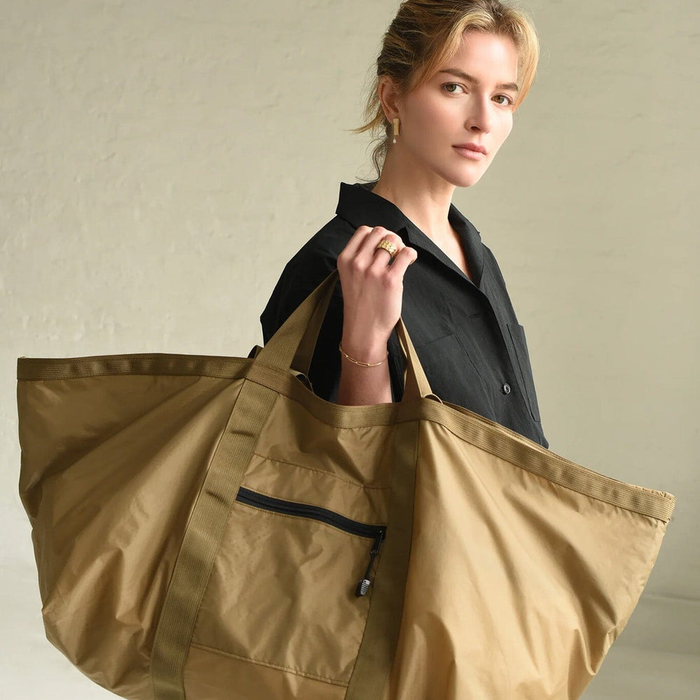 Woman holding a large brown tote bag against a neutral background