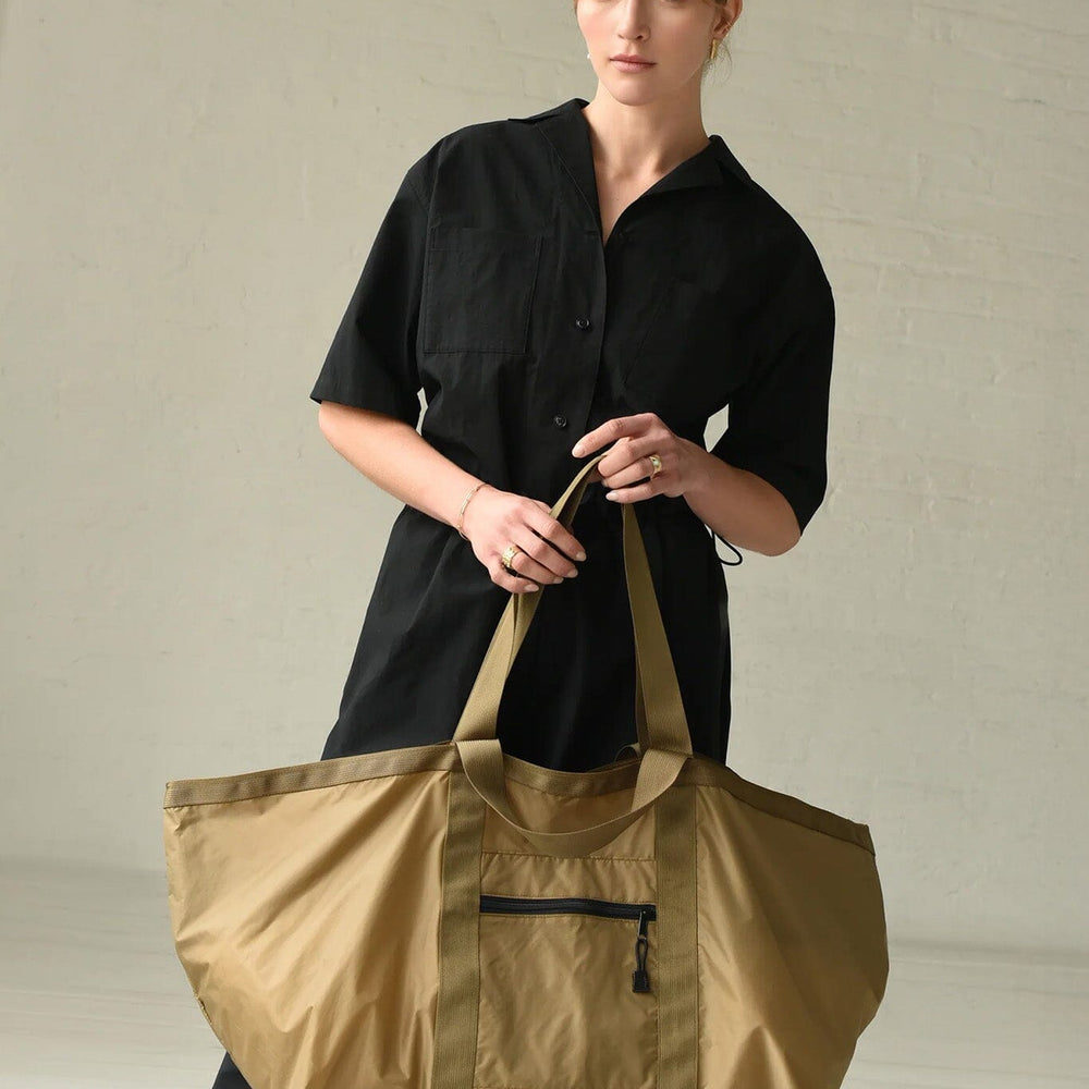 Woman holding a brown and green large tote bag against a plain background