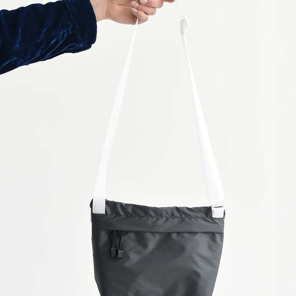 
                  
                    Black and white crossbody bag held by a person against a white background
                  
                