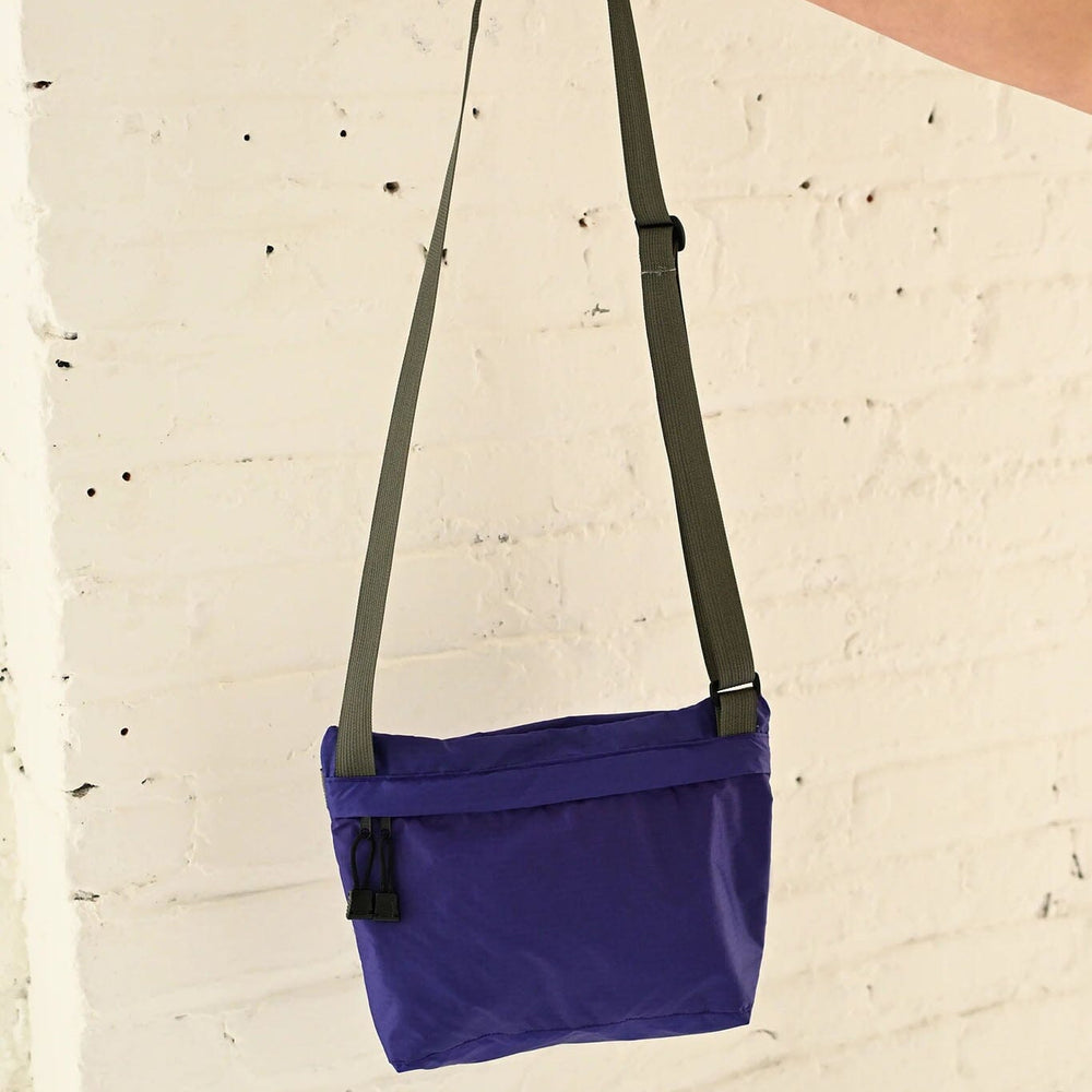 
                  
                    Purple shoulder bag with a strap held by a hand against a light beige background
                  
                