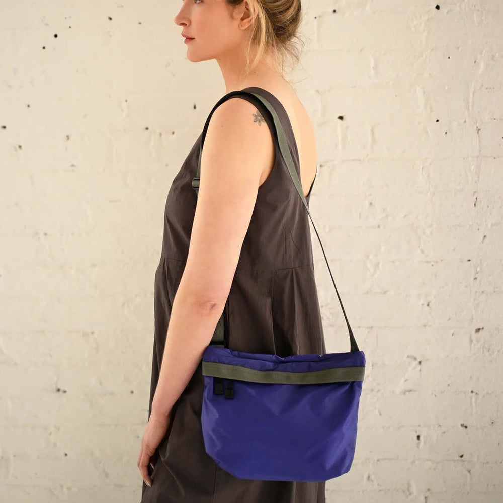 Woman wearing a purple crossbody bag against a textured white wall