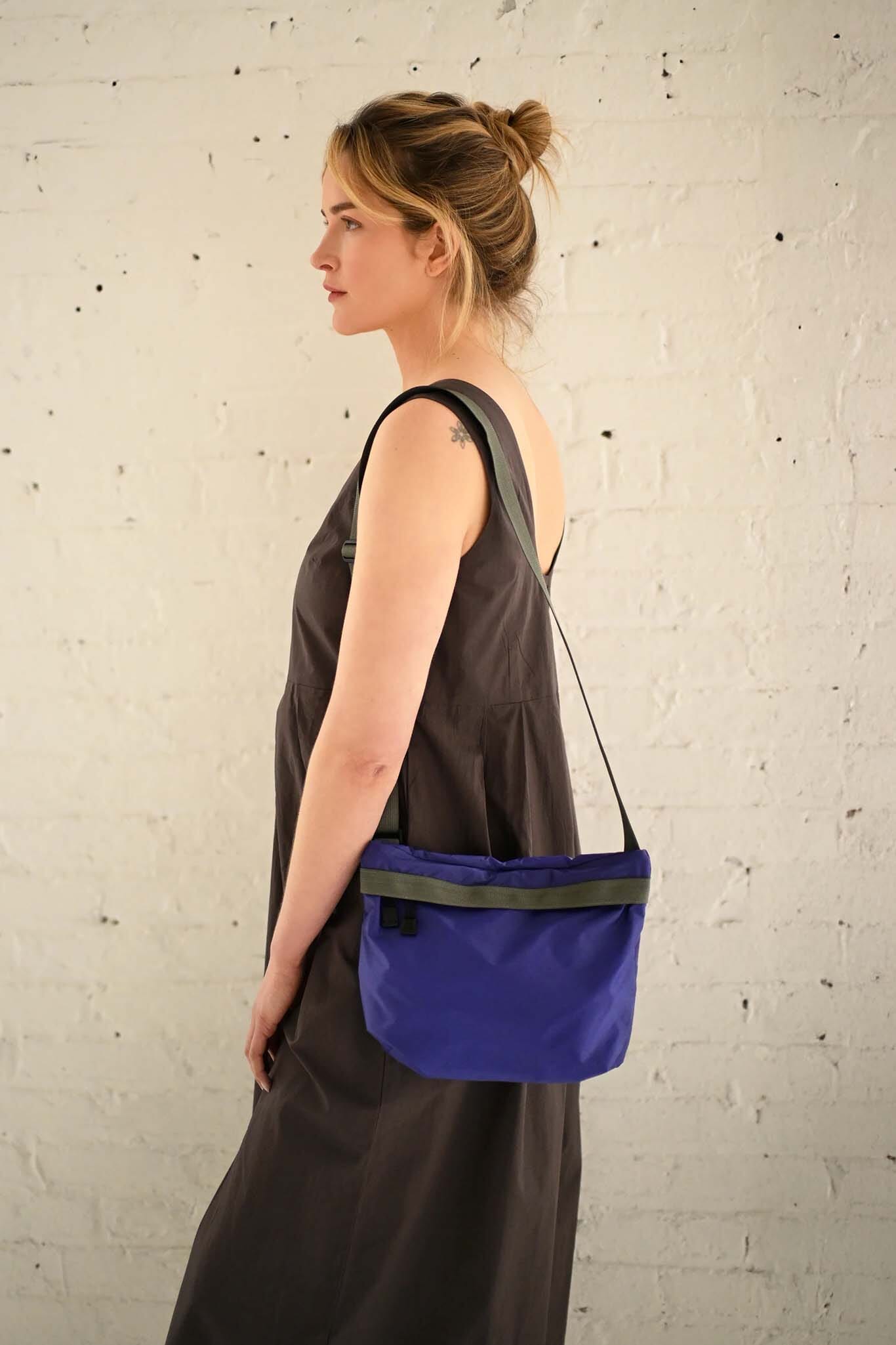 Woman wearing a purple crossbody bag against a textured white wall
