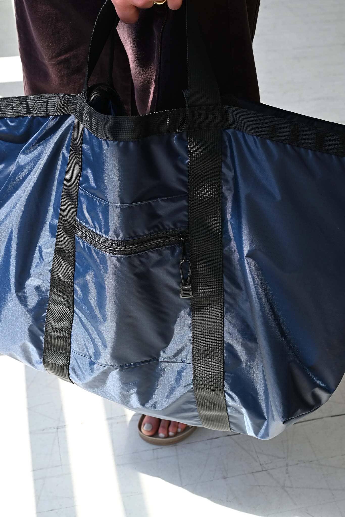 Blue bag with black straps held by a person, on a light-colored floor.