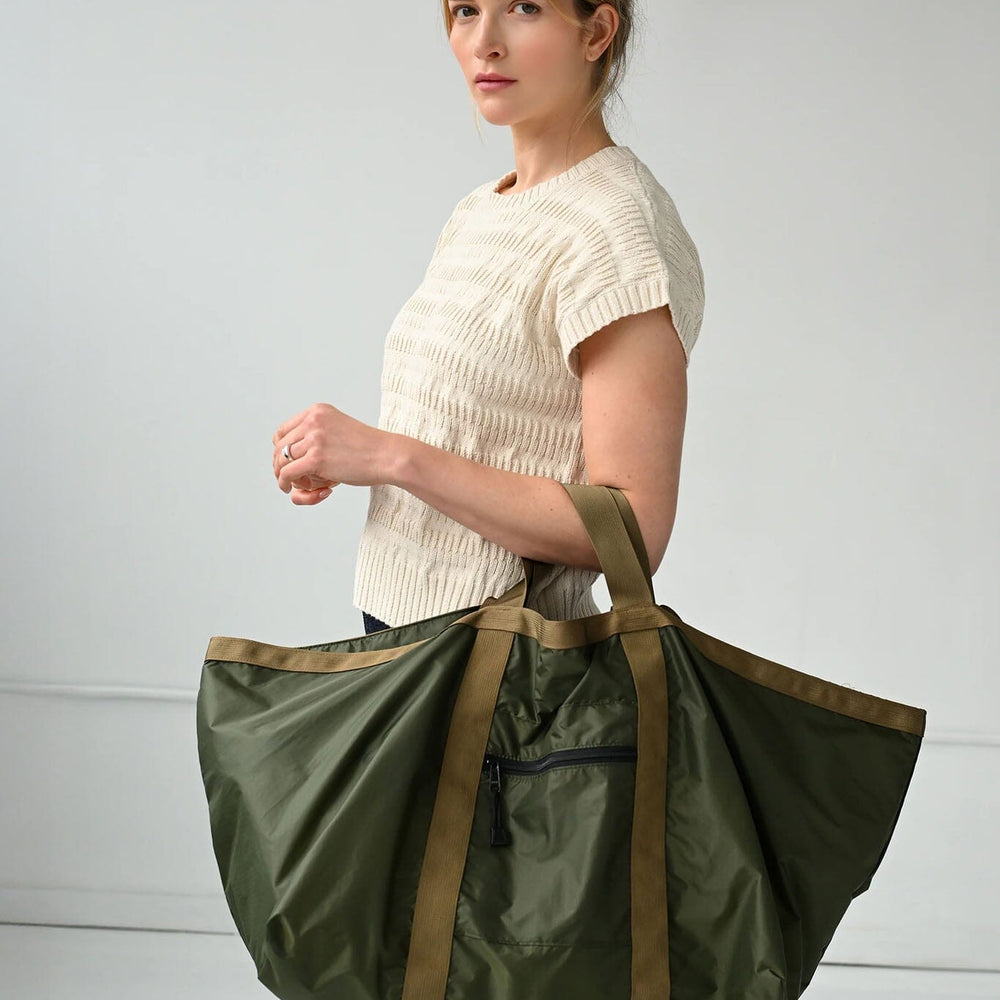 
                  
                    Woman holding a large green tote bag against a plain background
                  
                