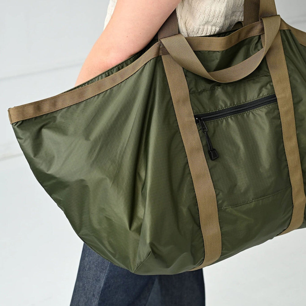 
                  
                    Person holding a green duffel bag with brown handles on a light gray background
                  
                