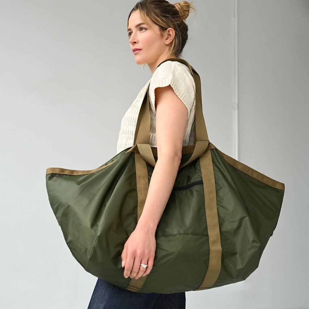 
                  
                    Woman carrying a large green and brown bag against a plain background
                  
                
