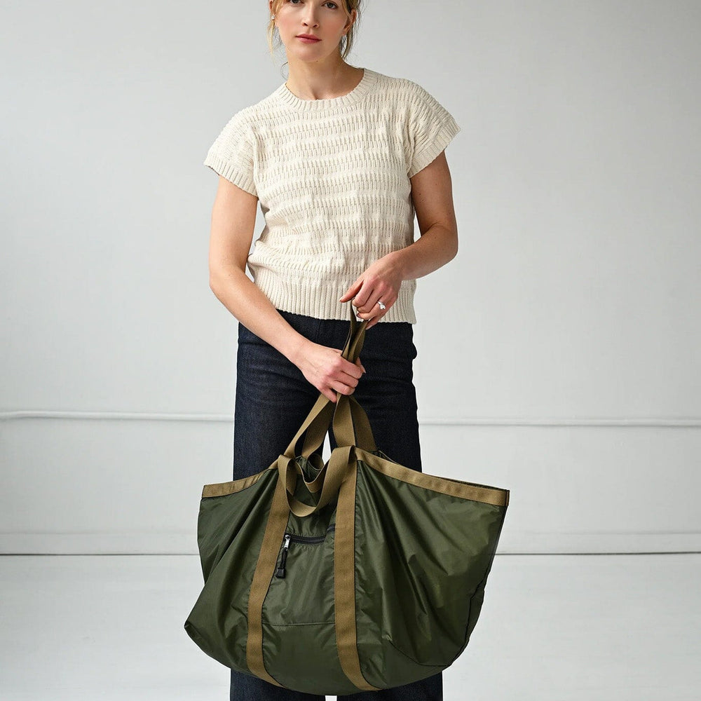Woman holding a large green tote bag against a plain background