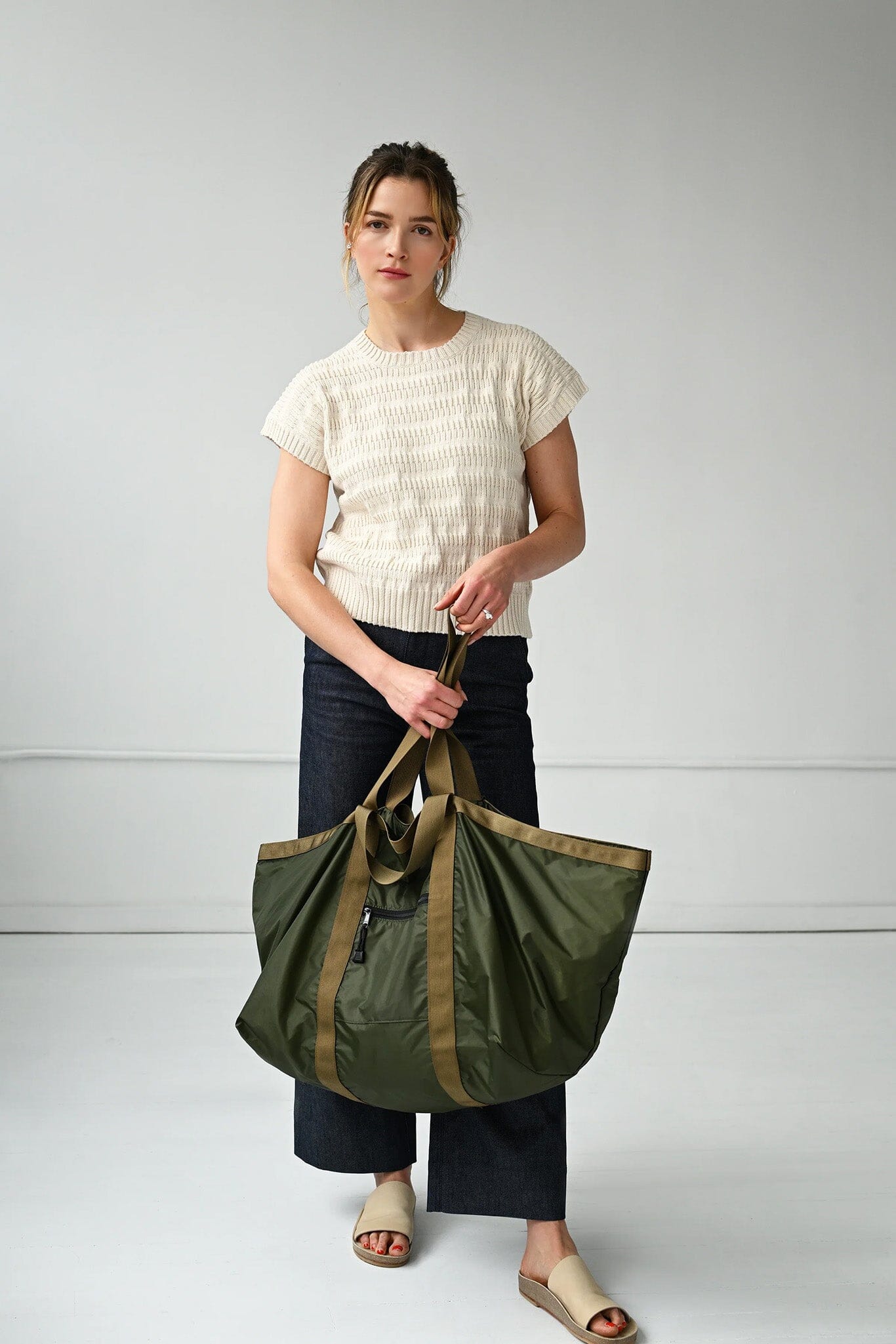 Woman holding a large green tote bag against a plain background