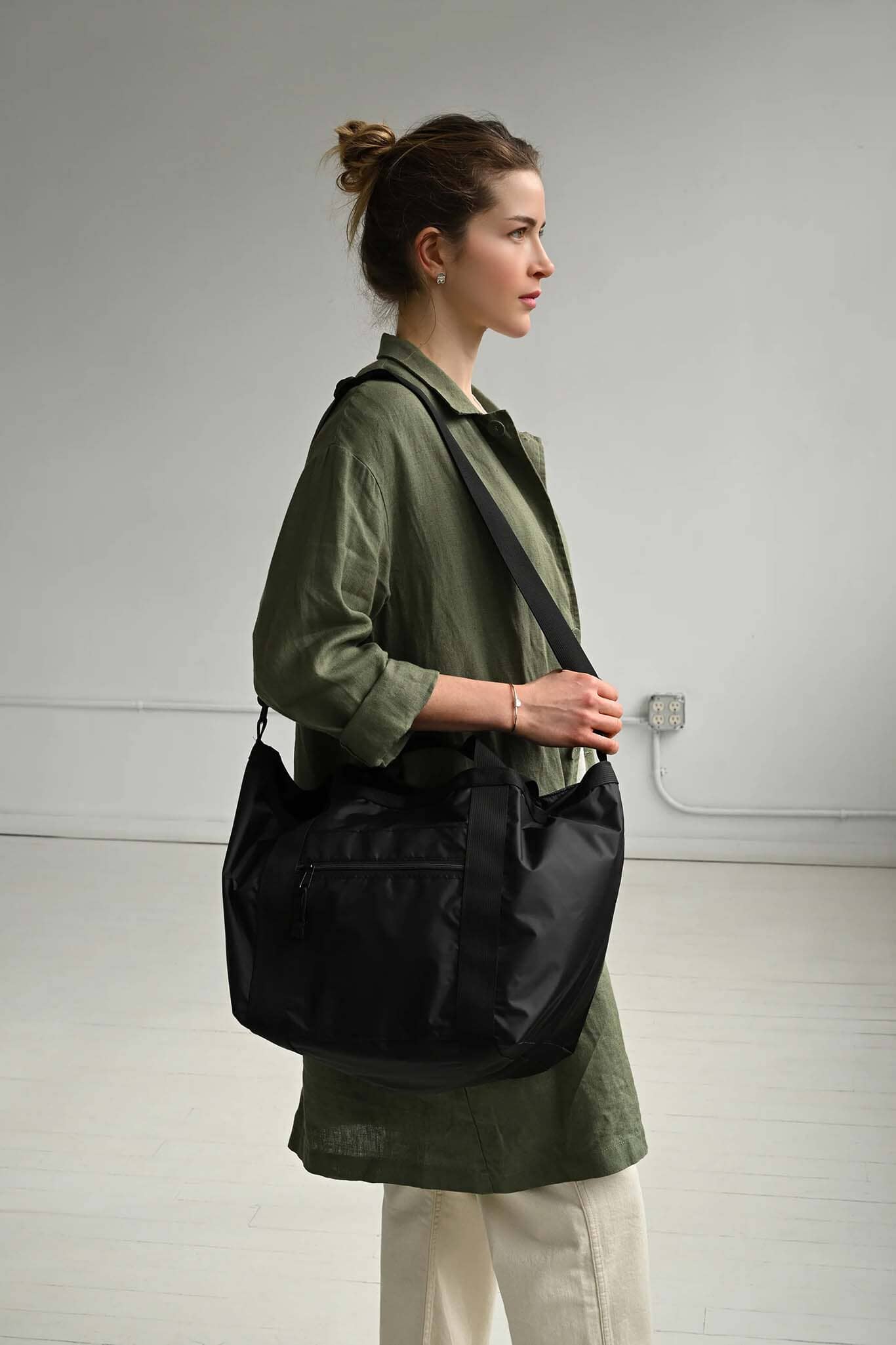Woman carrying a black bag over her shoulder in a minimalistic setting