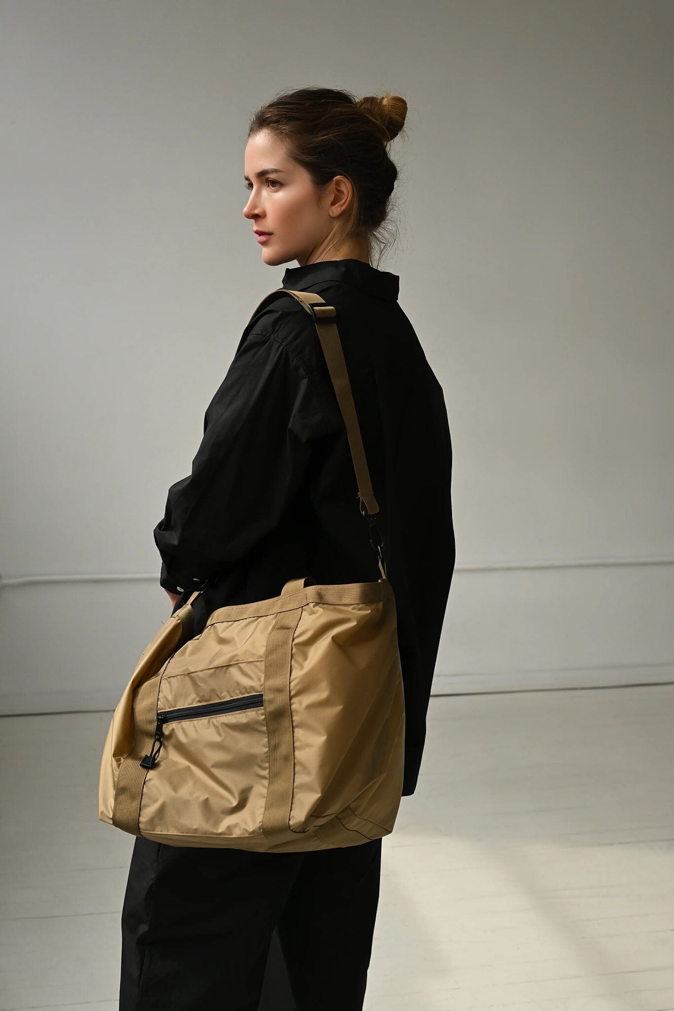 Woman wearing a beige shoulder bag against a plain background