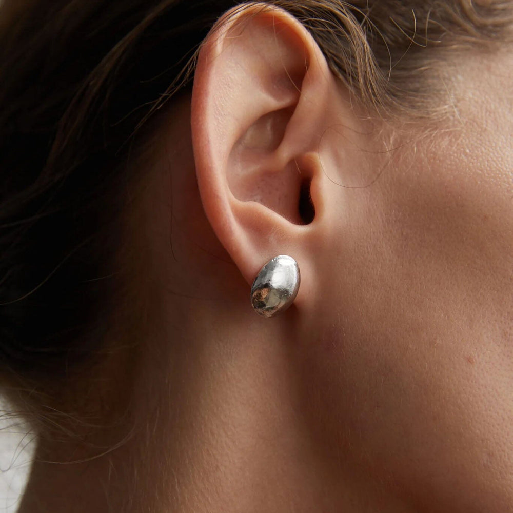 Close-up of a person wearing a silver dome stud earrings with a blurred background
