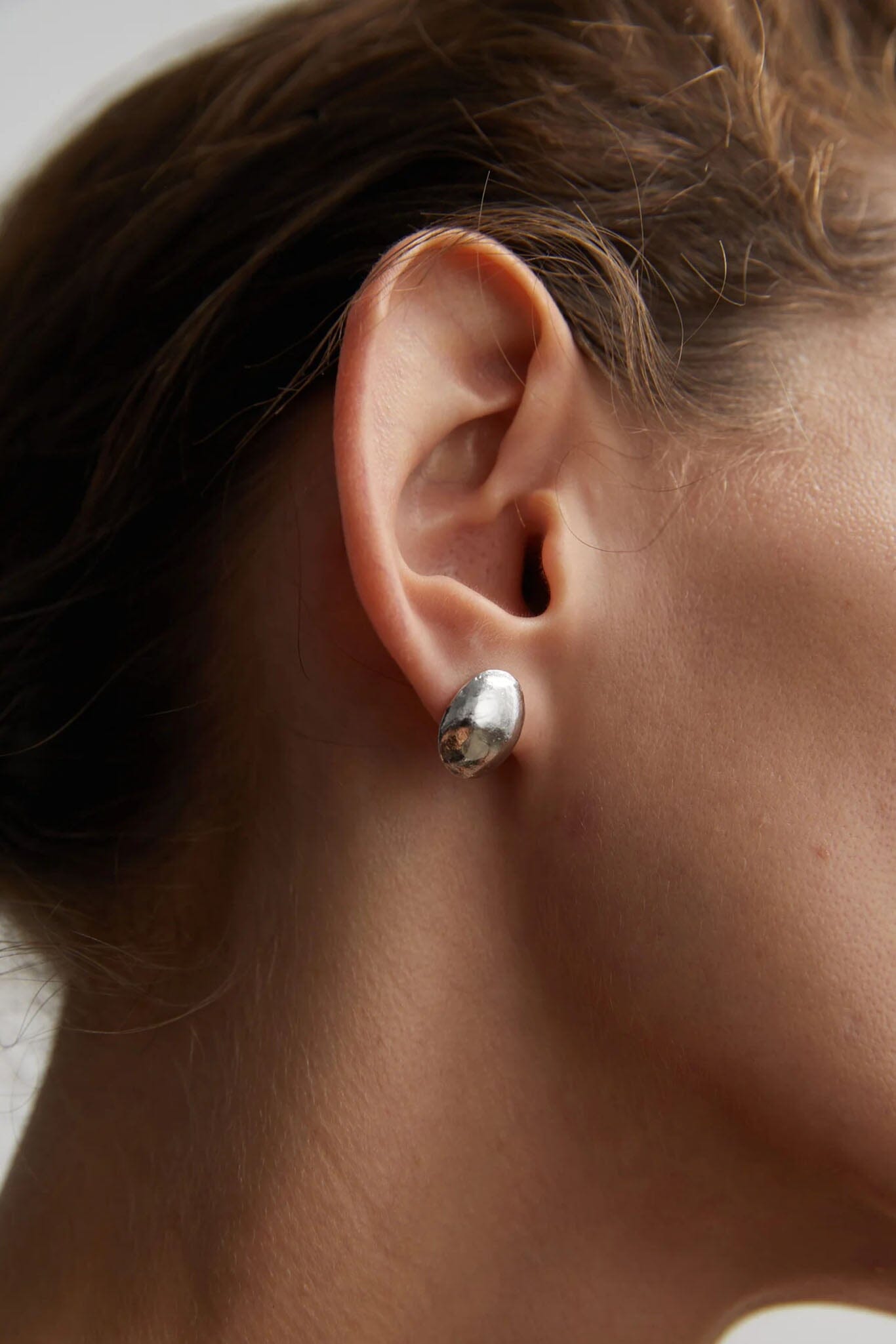 Close-up of a person wearing a silver dome stud earrings with a blurred background