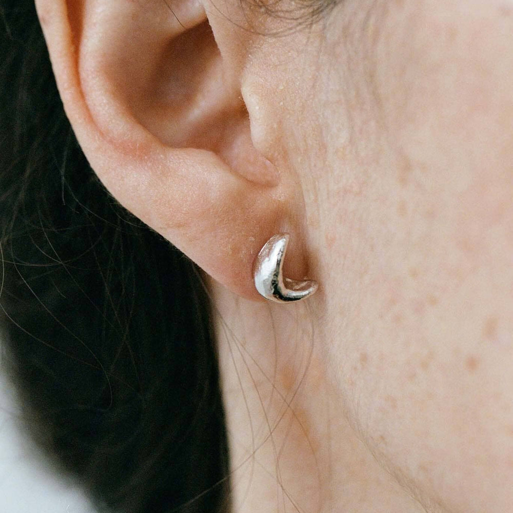 Close-up of a person wearing a silver crescent moon studs with a blurred background