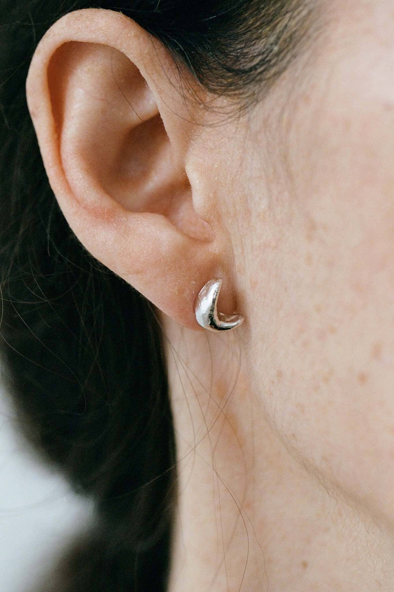Close-up of a person wearing a silver crescent moon studs with a blurred background