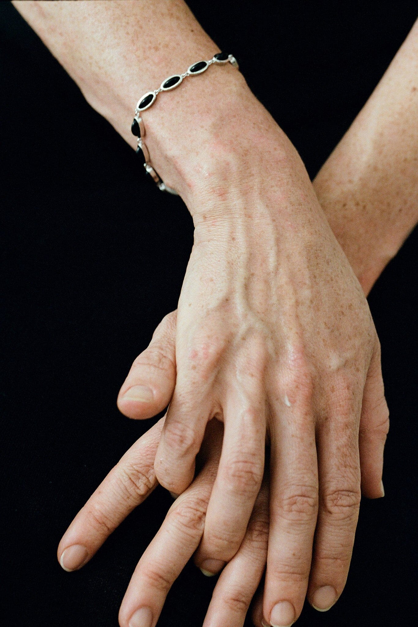 Close-up of hands with a black beaded bracelet on a black background