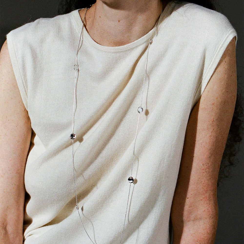 
                  
                    Woman wearing a cream sleeveless top with long sterling silver circle necklace against a dark background
                  
                