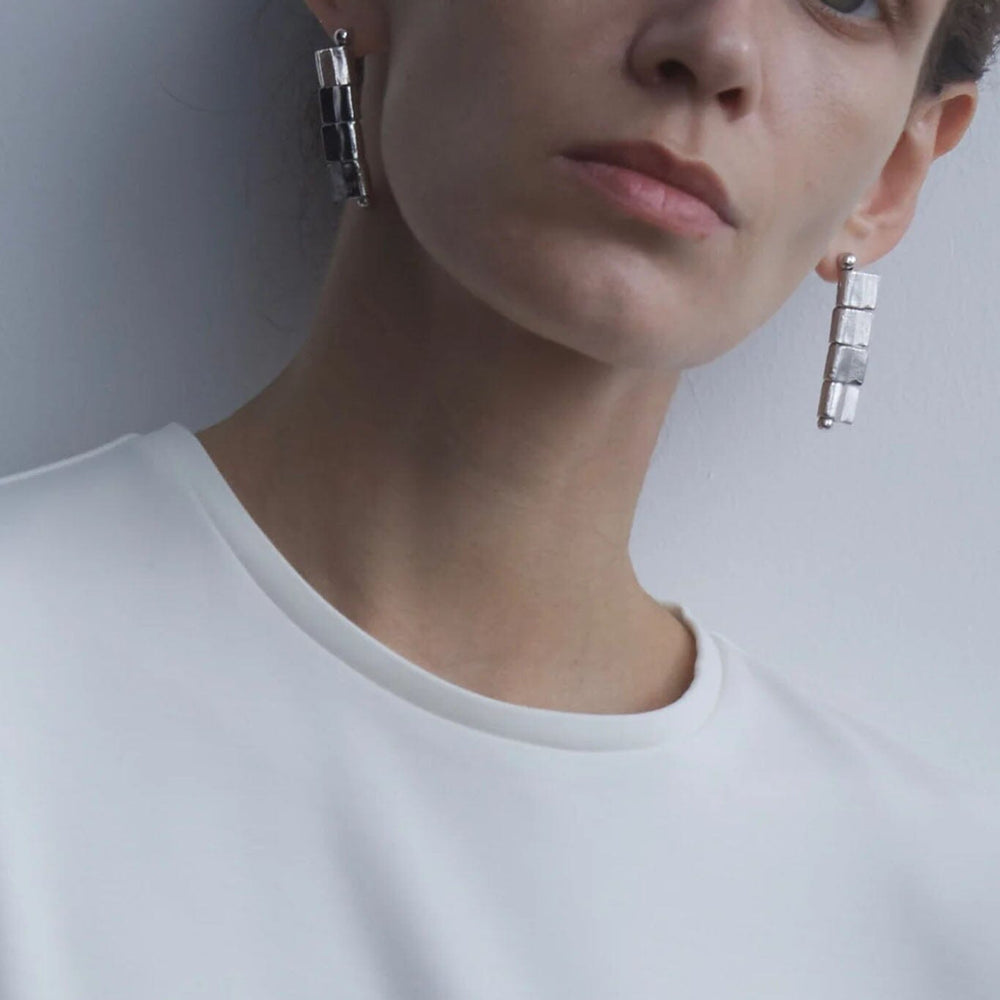 
                  
                    Person wearing silver earrings against a plain background
                  
                