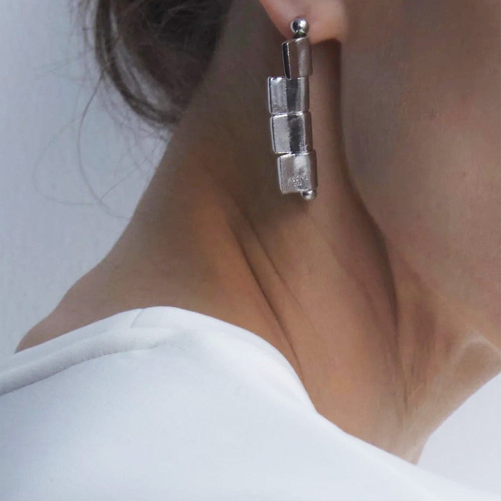 Close-up of a person wearing a silver drop earring with a neutral background