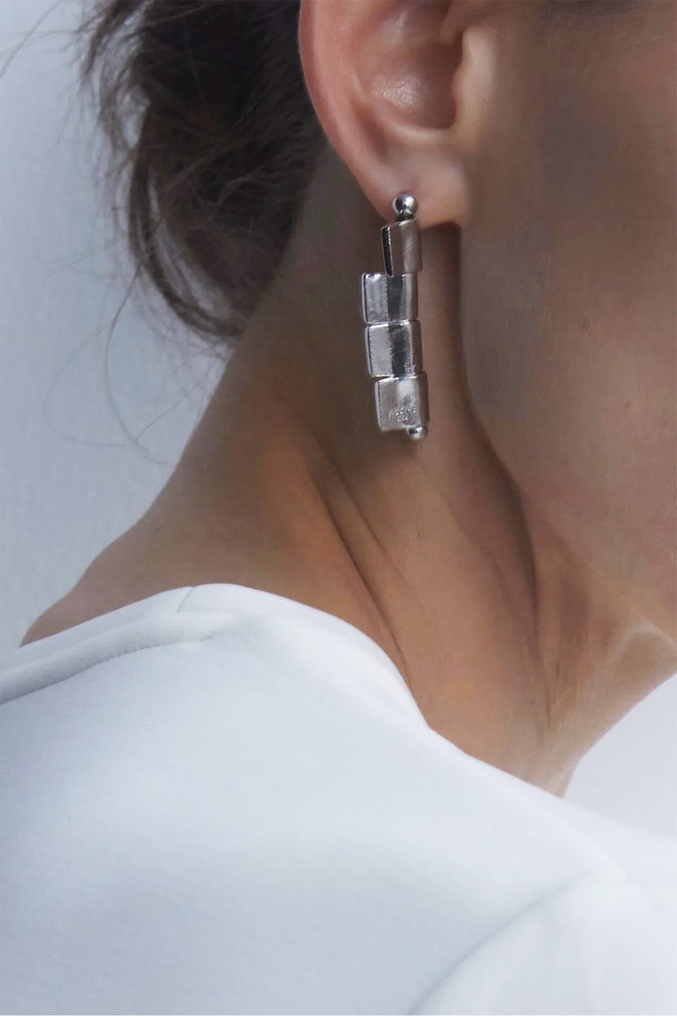 Close-up of a person wearing a silver drop earring with a neutral background