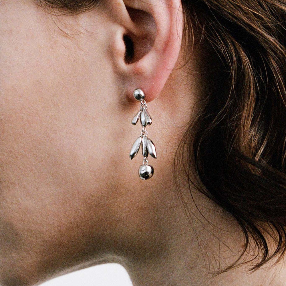 Close-up of a person wearing a silver drop earring with dangling beads on a neutral background