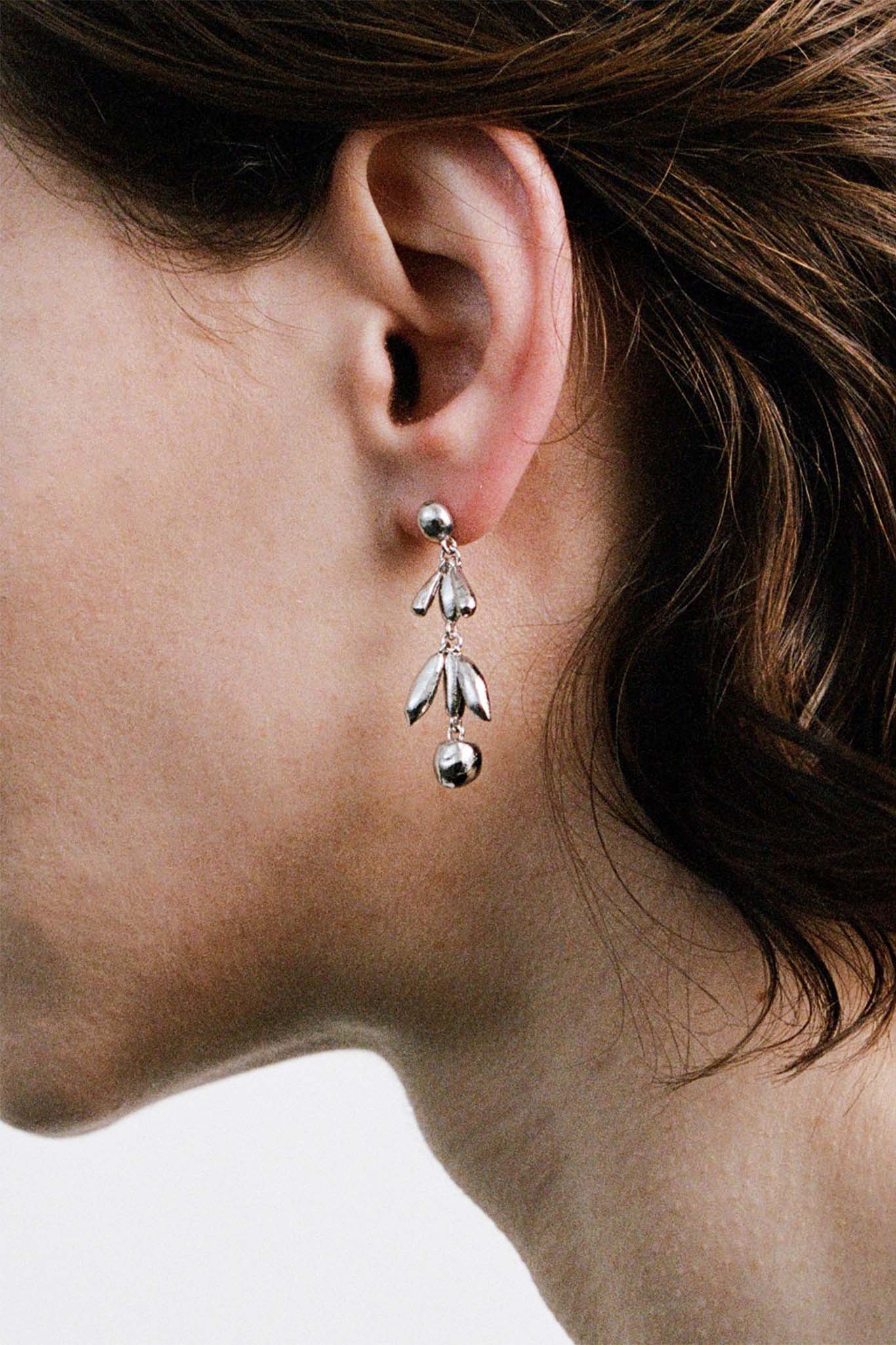 Close-up of a person wearing a silver drop earring with dangling beads on a neutral background