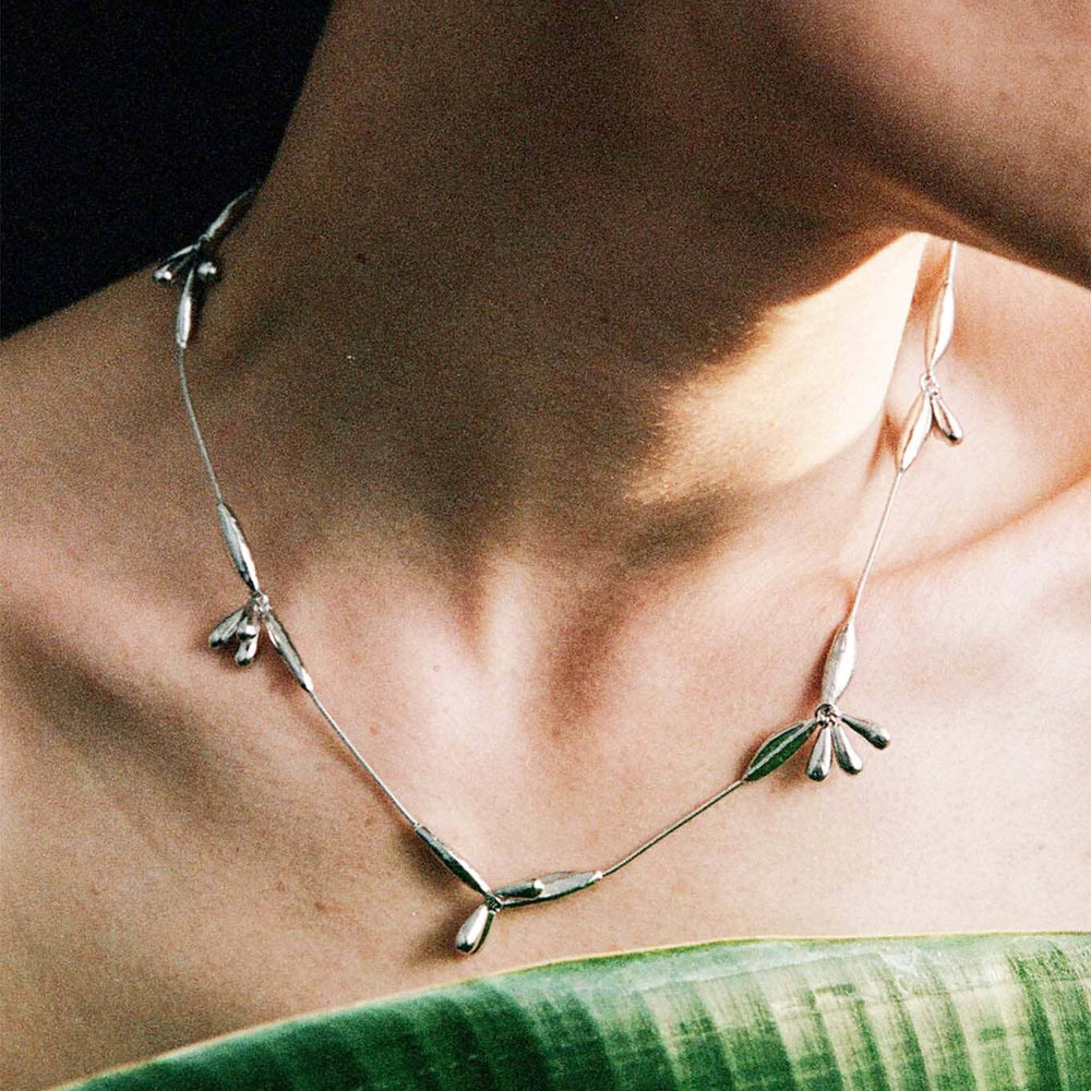 
                  
                    Necklace with leaf-like pendants worn by a person against a dark background
                  
                