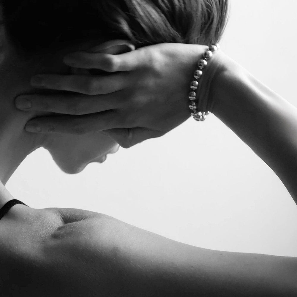 
                  
                    Person resting their hand on their head with a silver dome bracelet. 
                  
                