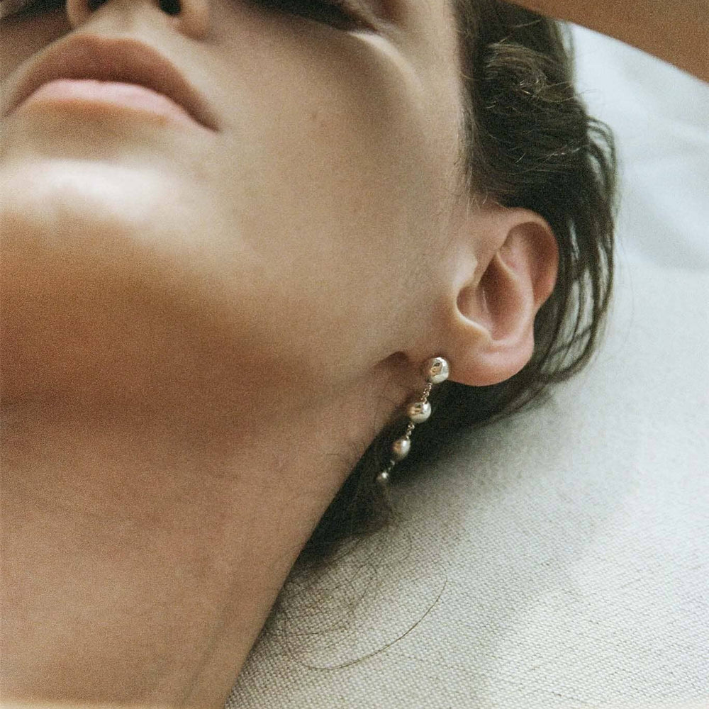 
                  
                    Close-up of a person wearing silver dome drop earrings on a blurred background
                  
                