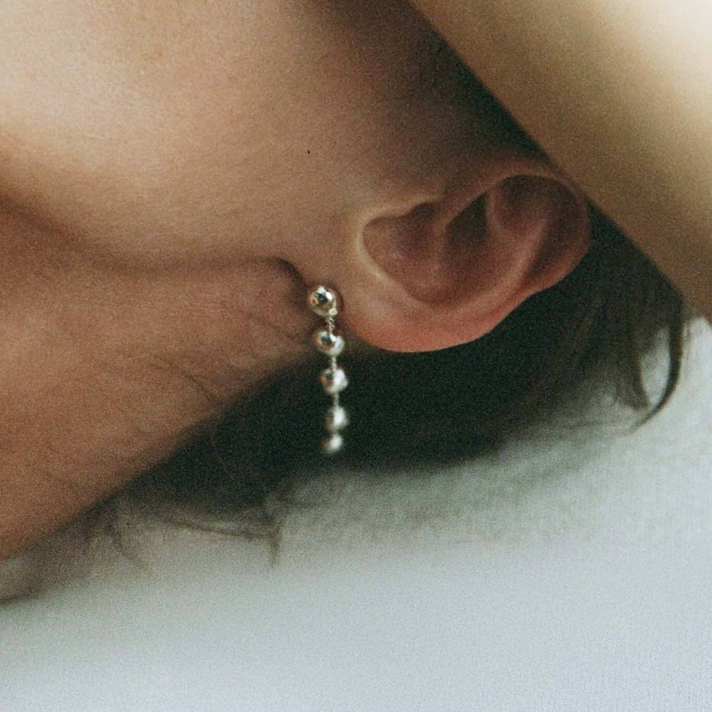 Close-up of an ear with a dome drop earring on a light background