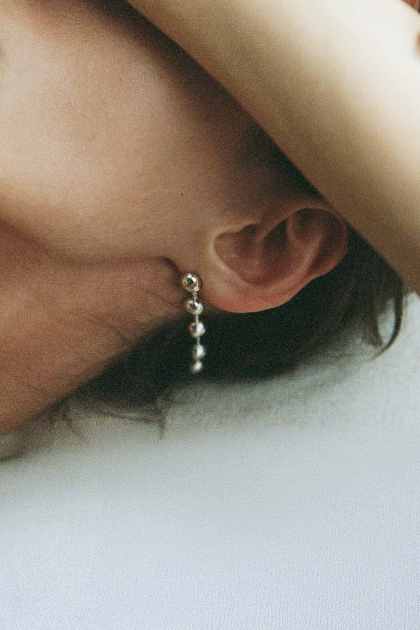 Close-up of an ear with a dome drop earring on a light background