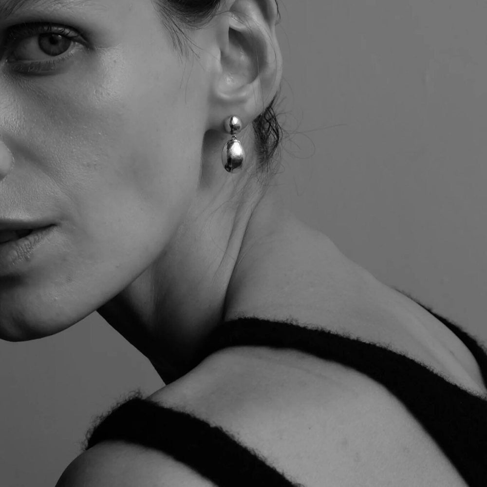 Black and white portrait of a woman wearing silver drop earrings with a plain background