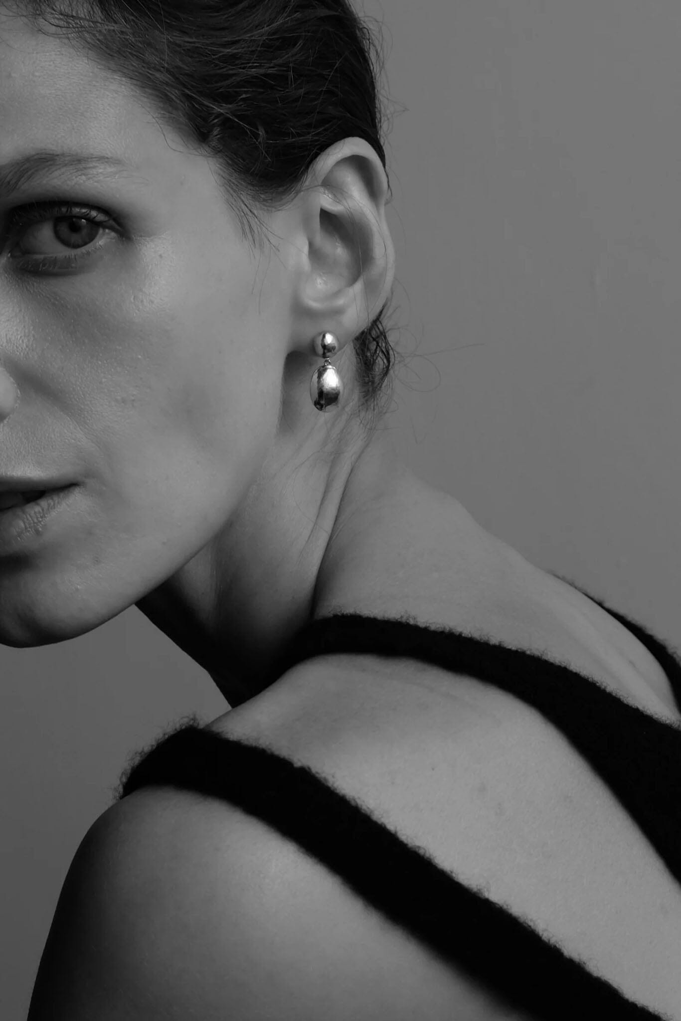 Black and white portrait of a woman wearing silver drop earrings with a plain background