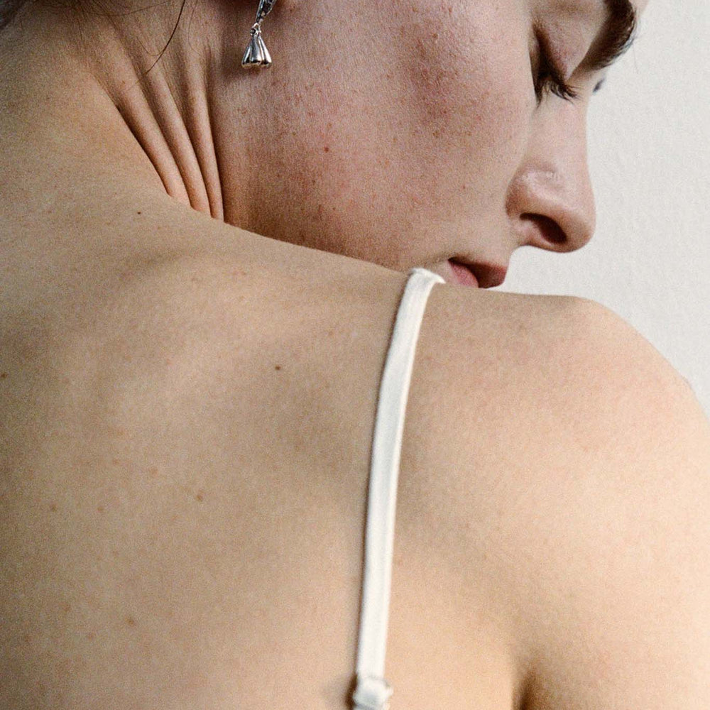 
                  
                    Close-up of a woman wearing silver floral drop earrings against a neutral background
                  
                