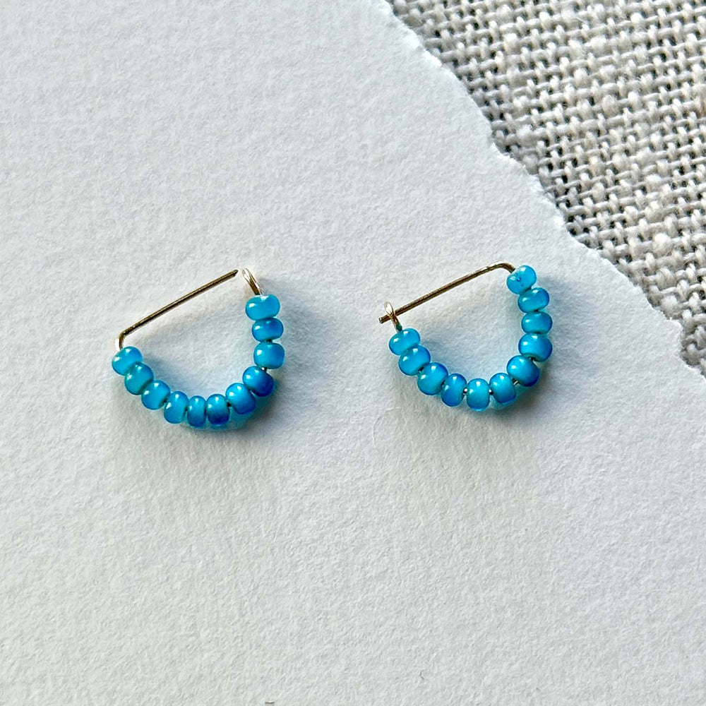 Pair of turquoise beaded hoop earrings on a light gray surface
