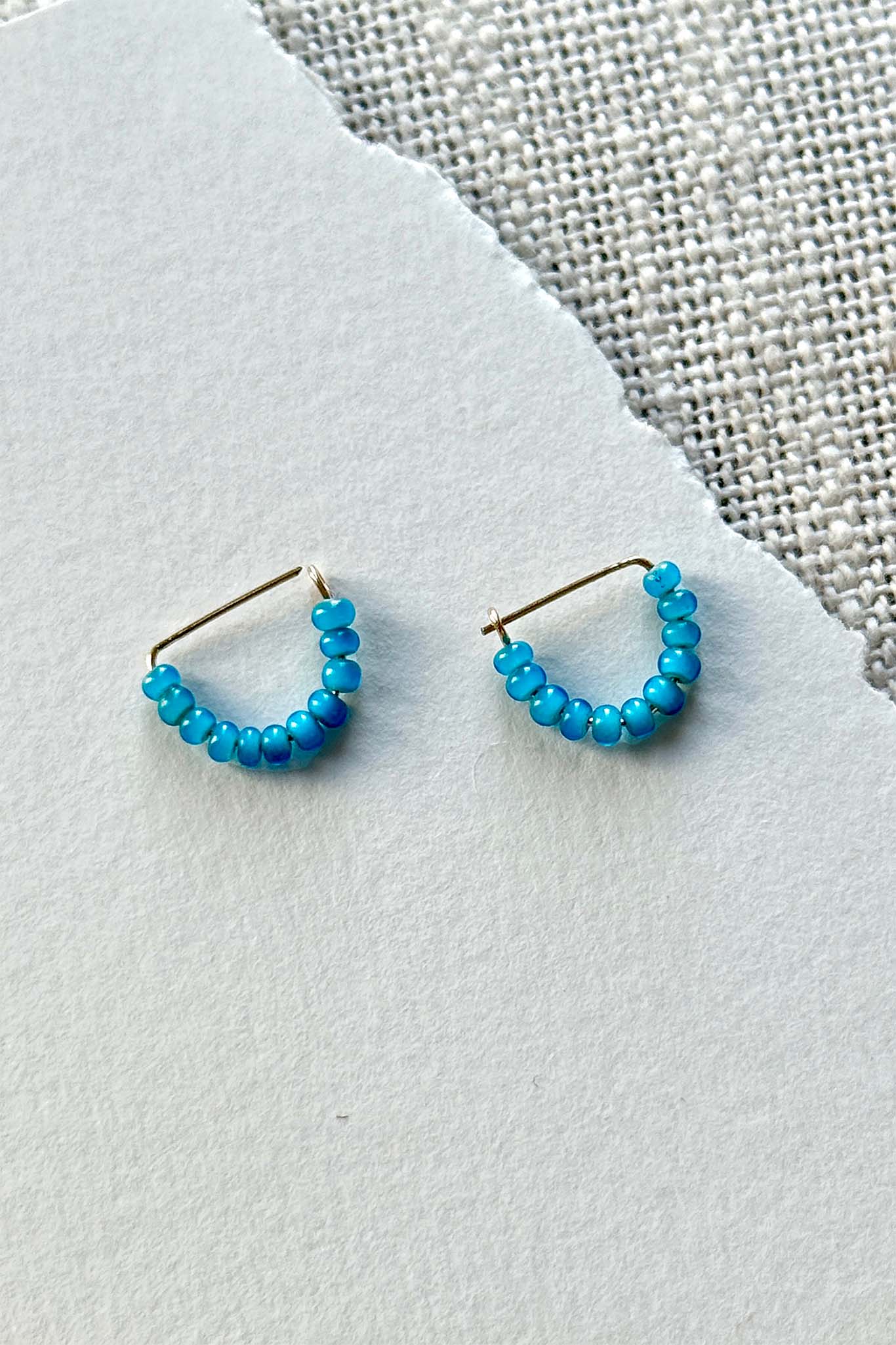 Pair of turquoise beaded hoop earrings on a light gray surface