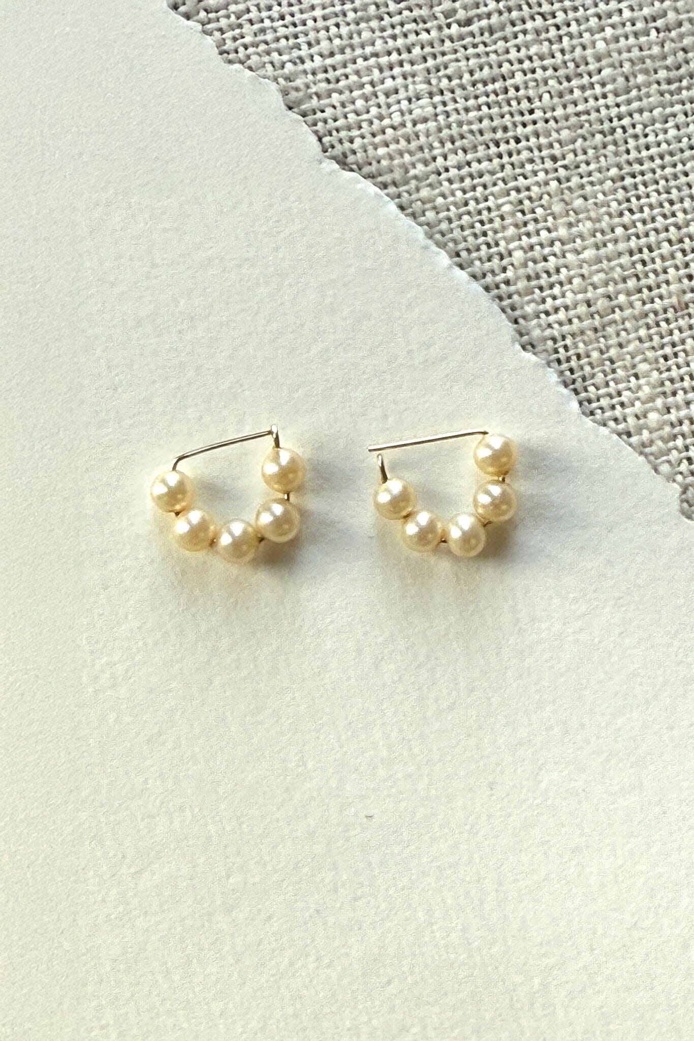 Pair of pearl hoop earrings on a textured fabric background