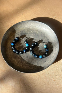 Dark blue beaded hoop earrings on a textured metal plate with a beige background