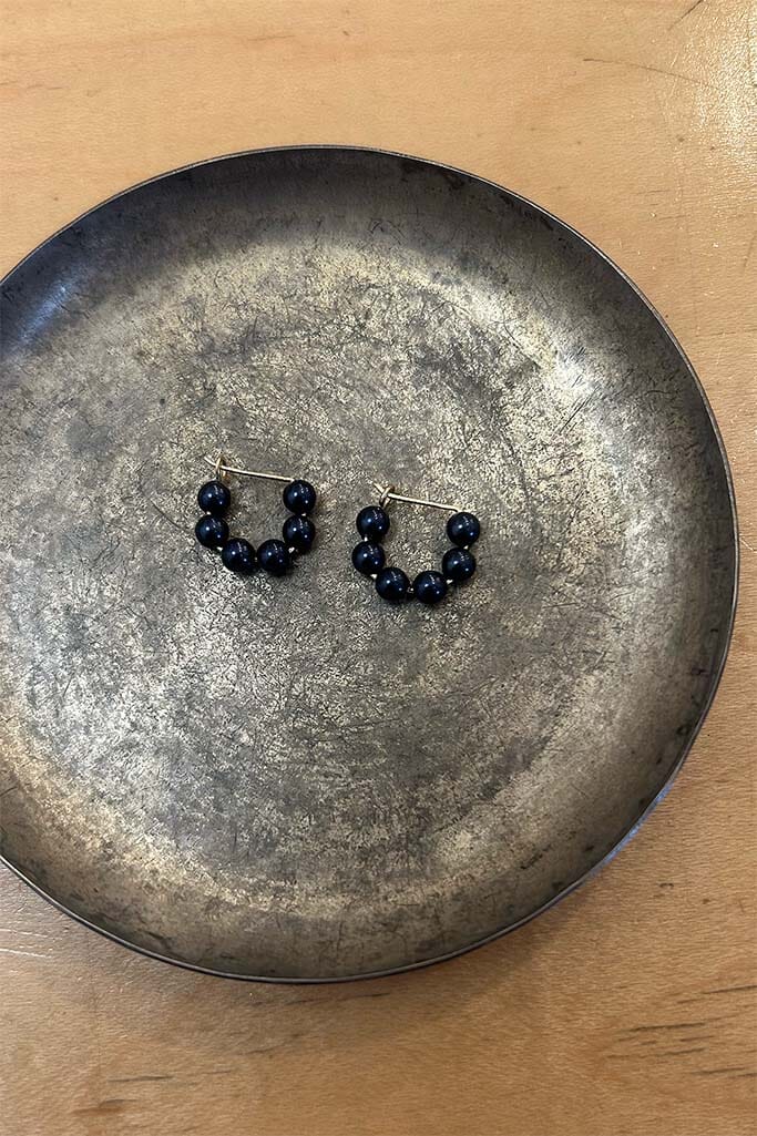 Pair of dark blue mini beaded hoop earrings on a metallic plate.