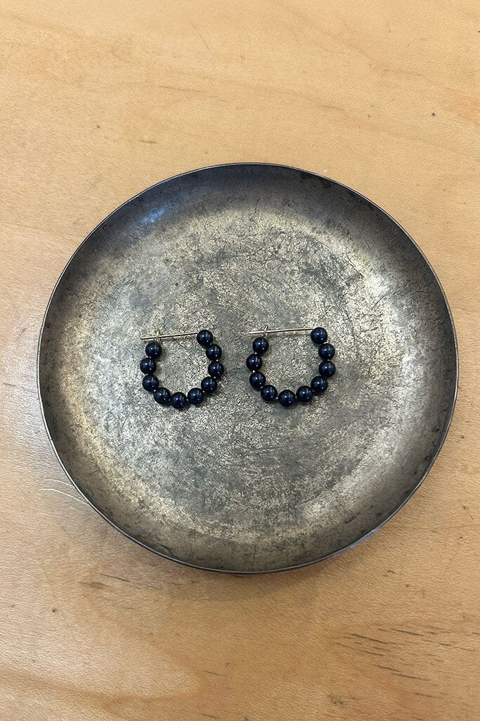 Pair of dark blue hoop earrings on a metallic plate with a wooden background