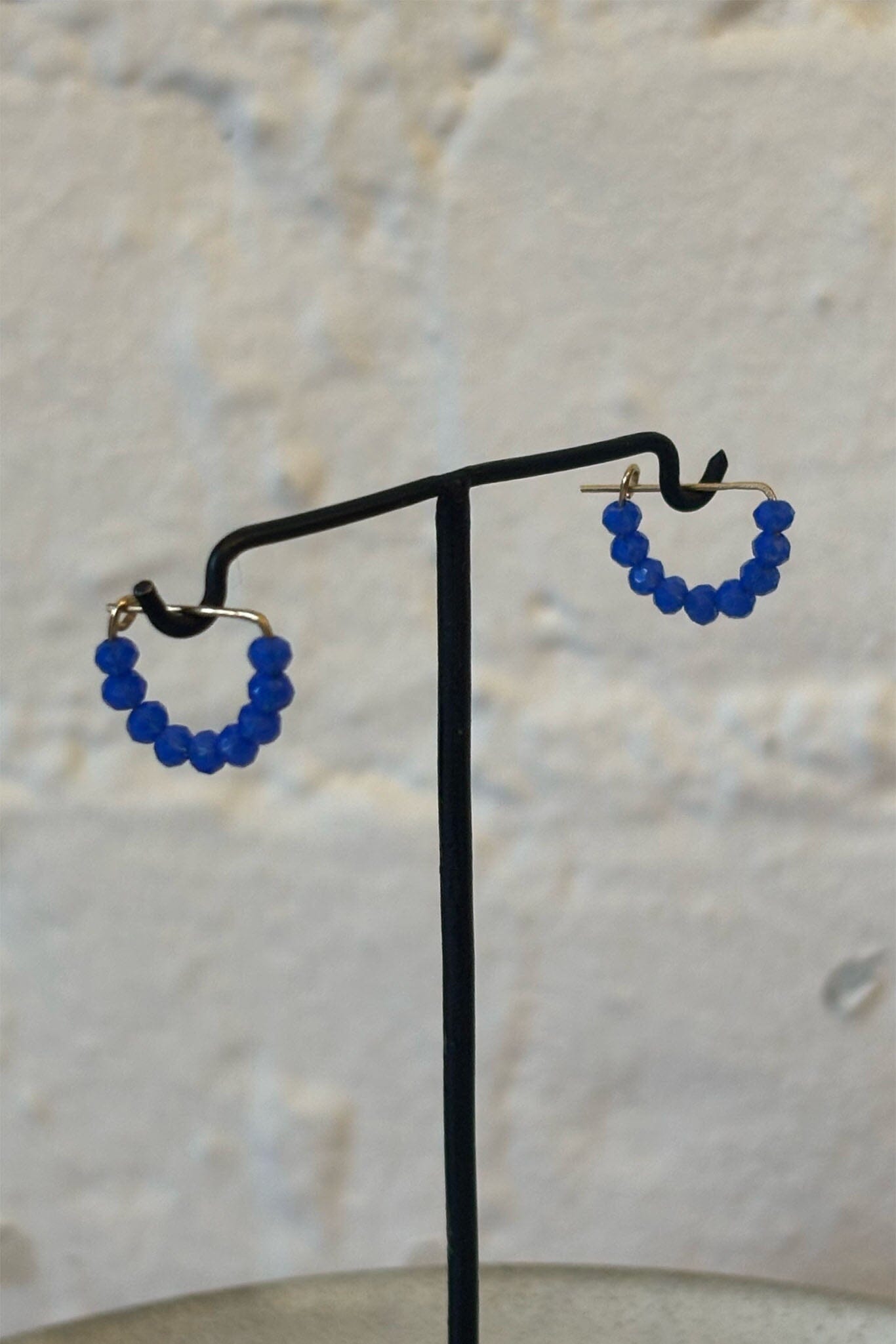 Blue beaded hoop earrings on a black stand against a light background