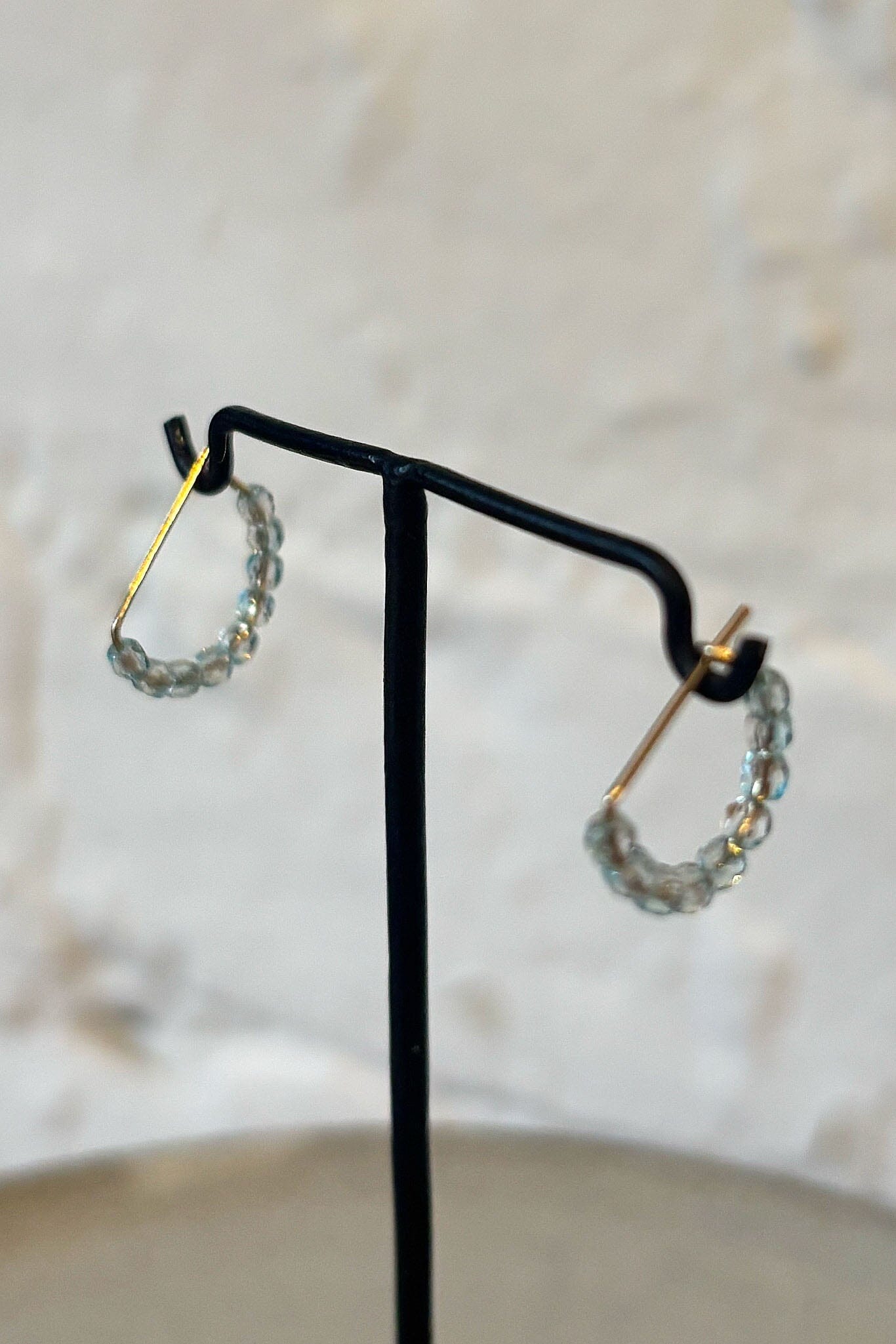 Pair of transparent blue hoop earrings on a black stand against a neutral background