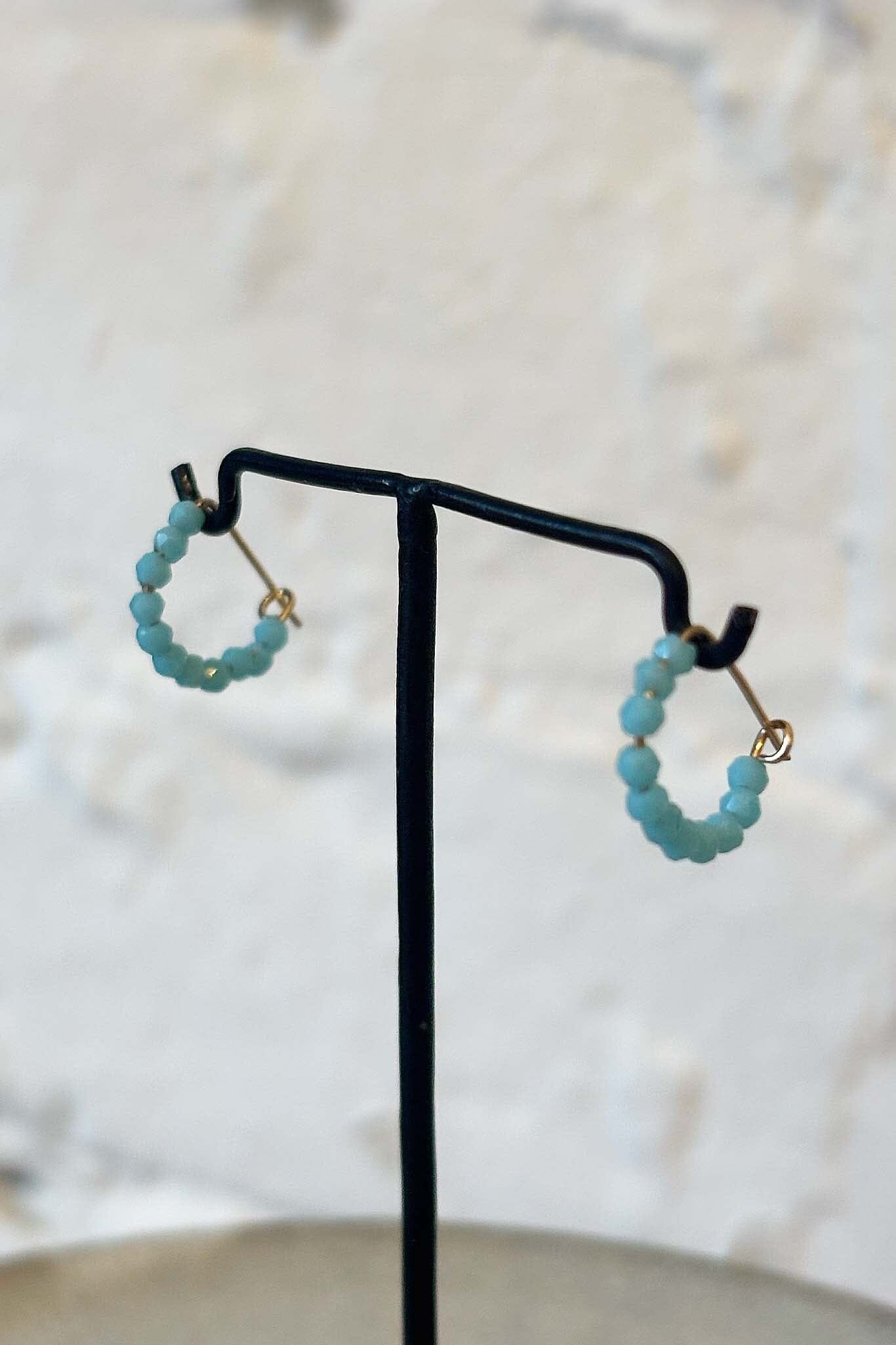 Turquoise beaded hoop earrings on a black earring stand with a blurred background