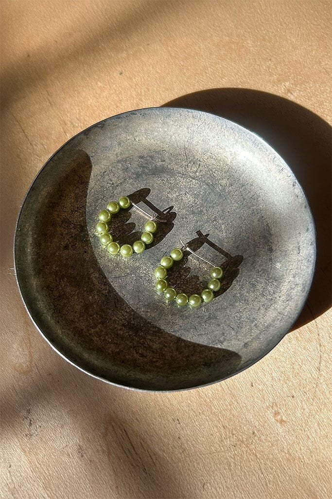 Pair of green pearl hoop earrings on a metallic surface with a beige background