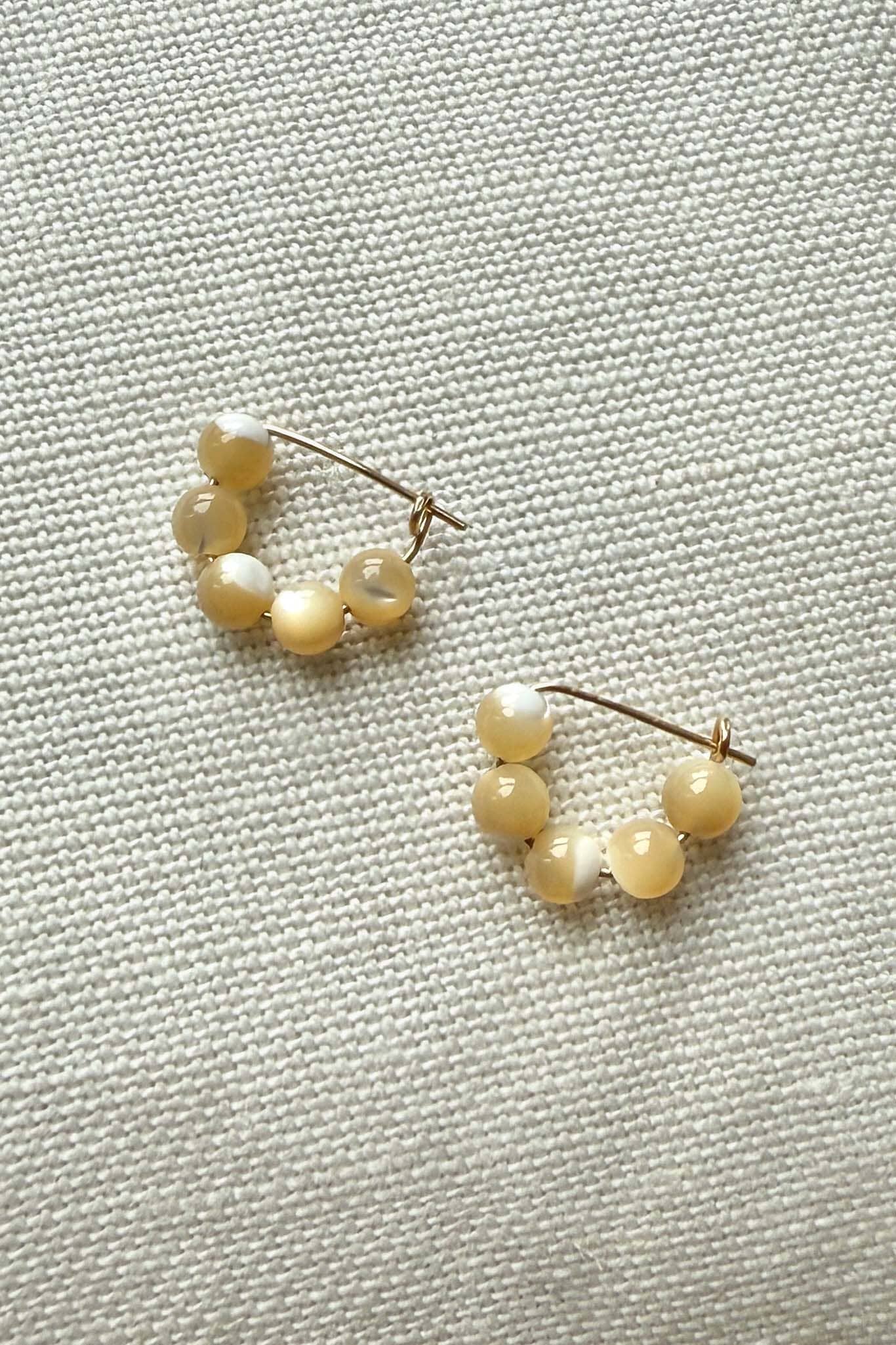 Pair of pearl hoop earrings on a textured fabric background