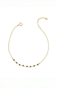 Gold bracelet with small black diamond beads on a white background