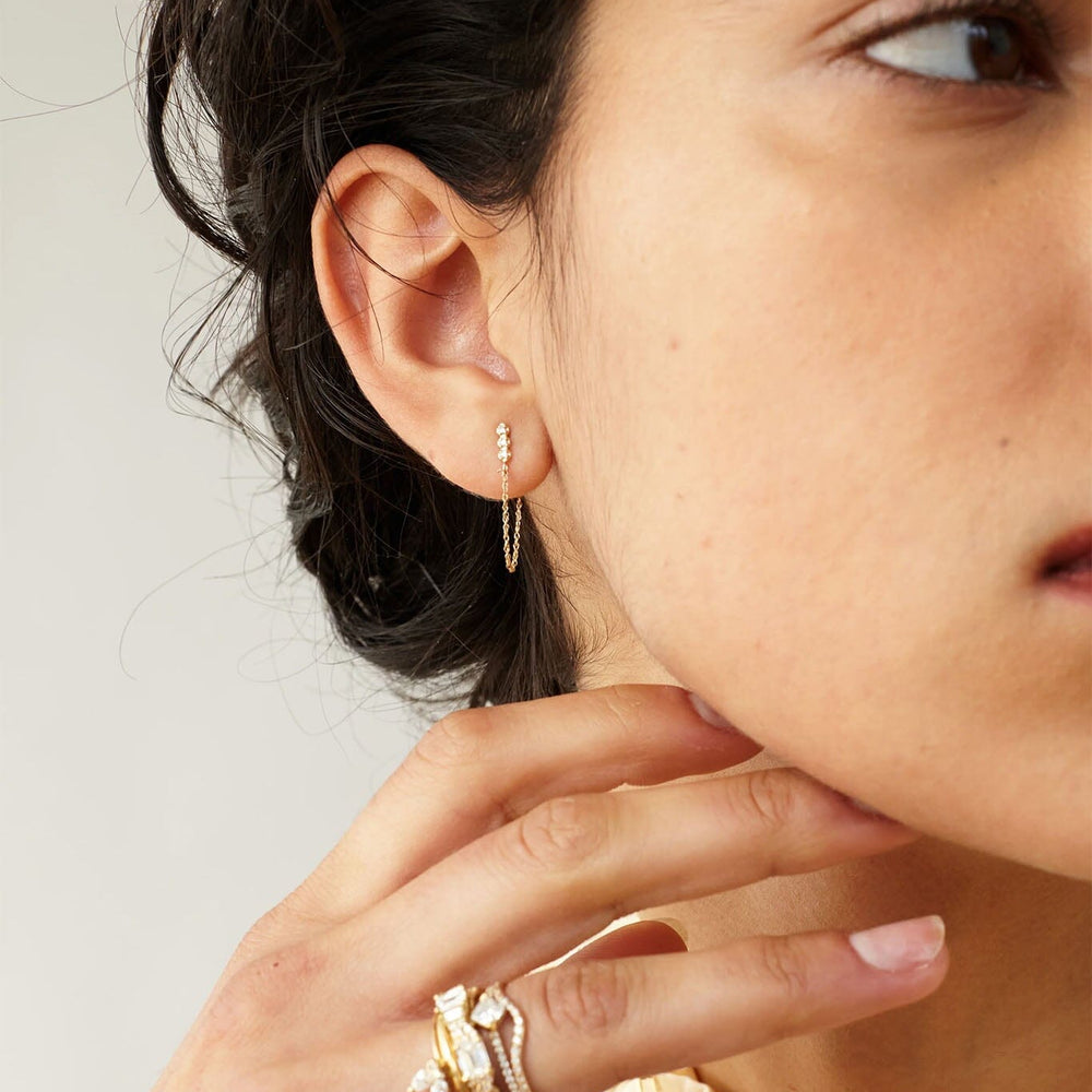 Close-up of a person wearing gold hoop earrings and rings on a neutral background
