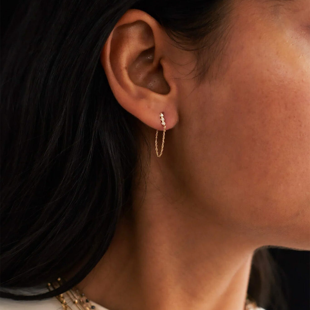 
                  
                    Close-up of an ear wearing a gold chain threader earring with layered necklaces.
                  
                