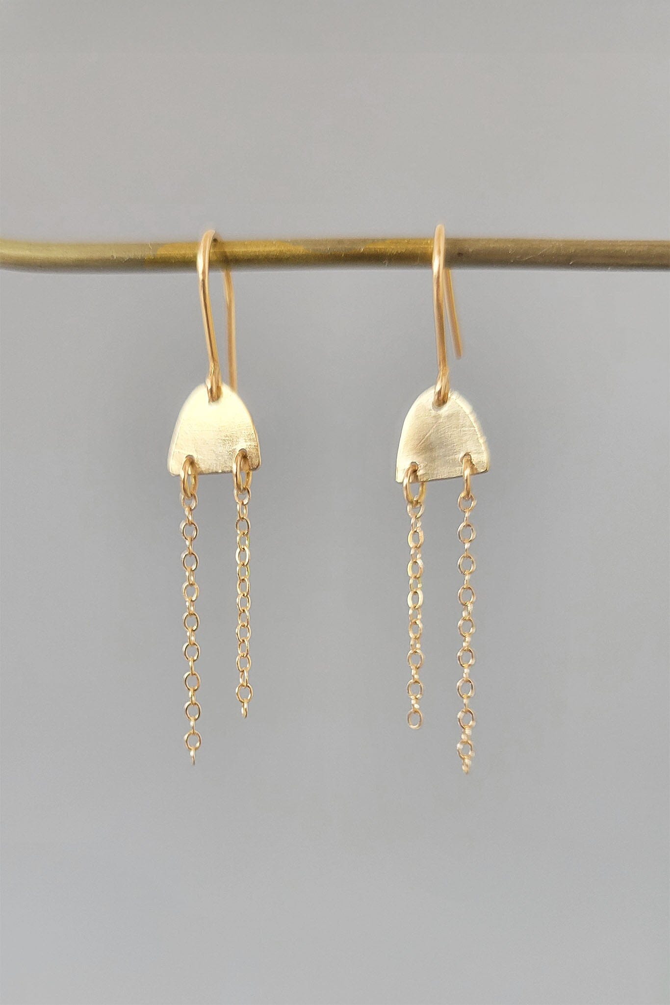 Gold earrings with chain drops on a gray background