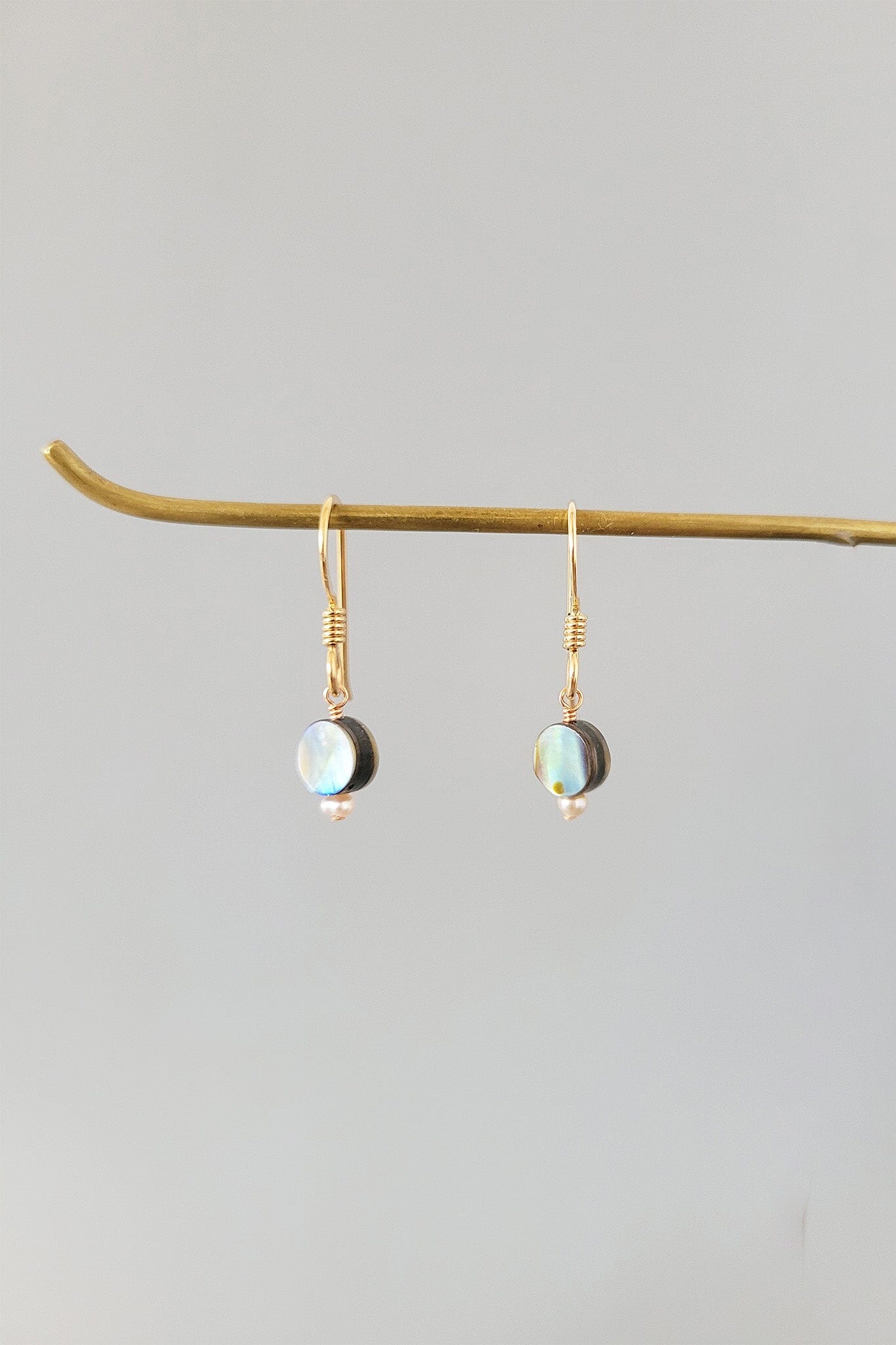 Gold earrings with opal stones on a branch against a light gray background