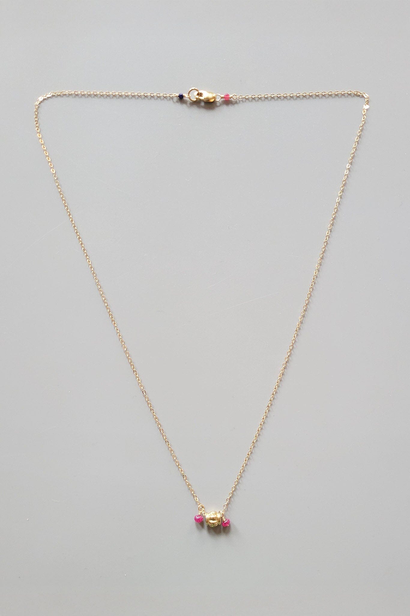 Gold necklace with a small gold pendant and ruby beads on a gray background
